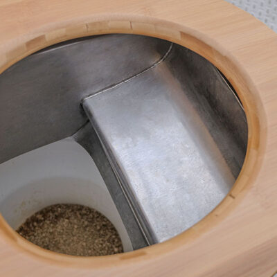 Detailansicht des Peepot-Systems in der Libre Trockentoilette mit Edelstahltrennblech und Holzsitz, darunter Auffangbehälter mit Einstreu.