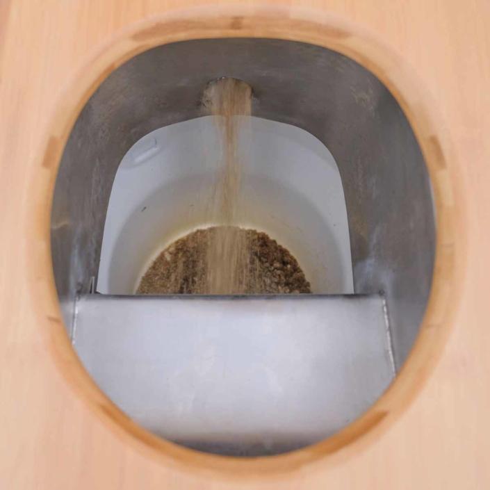 Toilette mit Urinableitung und angeschlossenem Streuspender. Streu rieselt durch Öffnung direkt auf die Feststoffe.
