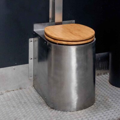 Detailansicht Soloo Trockentoilette mit Edelstahltoilette und Holzsitz auf rutschfestem Metallboden vor schwarzer Wand.