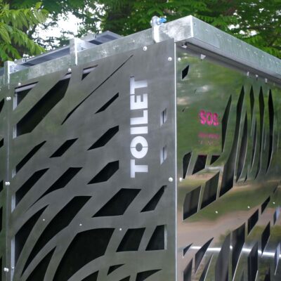 Außenansicht der Libre-DIN Kabine mit Edelstahlverkleidung, beleuchtetem TOILET-Schild und SOS-Logo bei SOS-Notknopfdruck.