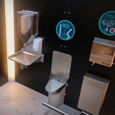 Innenansicht der Libre-DIN Kabine mit Unisexurinal, Papierspender, Handwaschstation und Abfallbehälter.