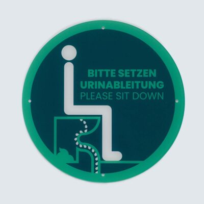 Rundes Hinweisschild aus Acrylglas mit grünem Rand, Piktogramm und Text „Bitte setzen Urinableitung – Please sit down“.