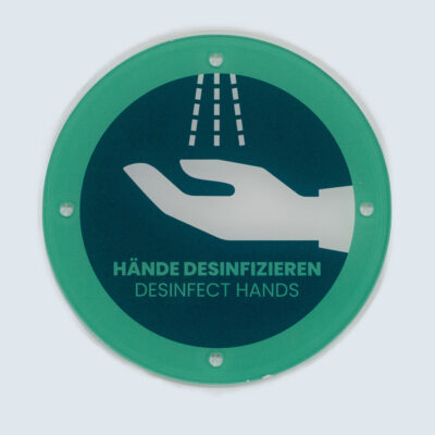 Rundes Acrylglasschild mit grünem Rand, Text „Hände desinfizieren – Desinfect hands“ und Piktogramm einer Hand unter Desinfektionsspray.