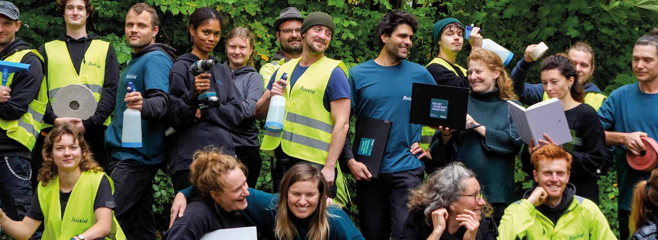 Mitarbeiter von Finizio in Arbeitskleidung mit Werkzeug, Reinigungsutensilien und Laptop.