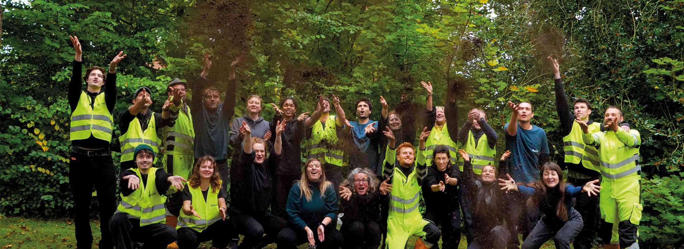 Die Crew in Warnwesten wirft Humusdünger aus Inhalten von Trockentoiletten in die Luft vor grünem Wald