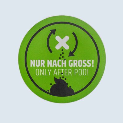 Rundes grünes Schild mit schwarzem Piktogramm und Text „Nur nach Groß!/ Only after poo!“.