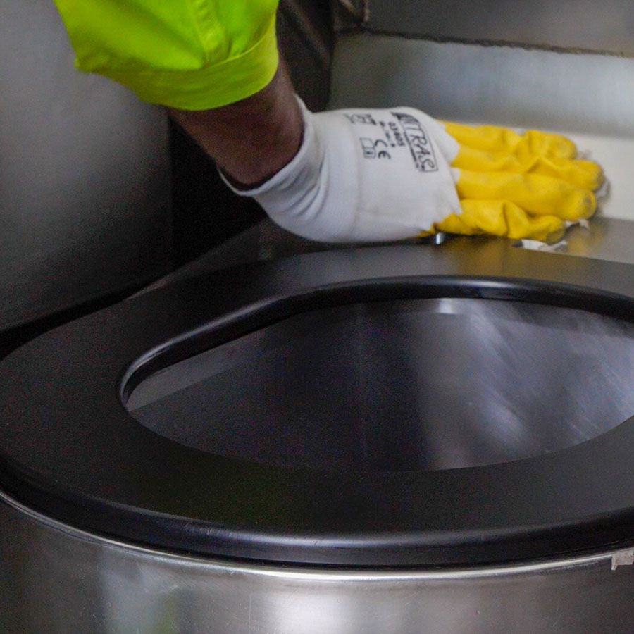 Schwarze Klobrille auf Edelstahl-Pee-Pot wird im Rahmen von Service und Reinigung mit gelbem Handschuh gepflegt.