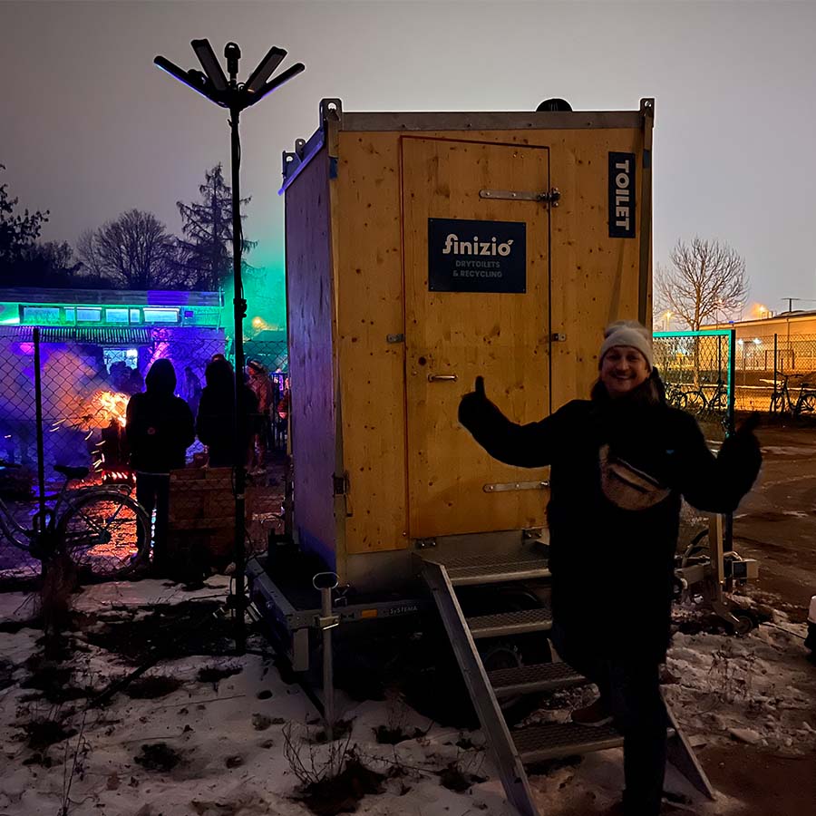 Ein Mensch vor einer Toilettenkabine aus Holz auf schneebedecktem Boden.